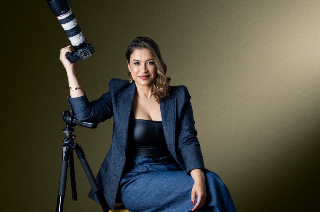 Ingrid Guimarães sentada, segurando uma câmera ao lado do tripé