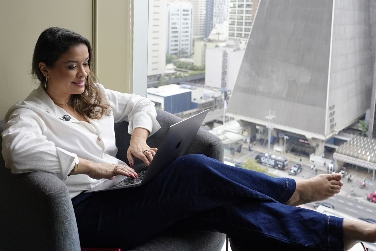 Ingrid trabalhando no notebook, sentada junto à janela